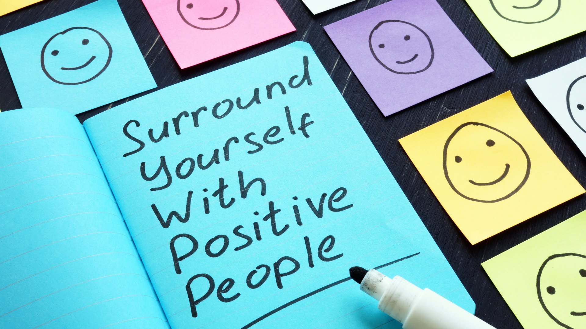 surround yourself with positive people written on blue paper surrounding by happy faces on sticky notes